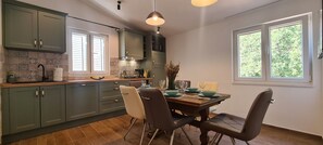 A kitchen with green cabinets, a dining table with chairs, and a window with a view of trees. - Apartments Hvaranin (Stari Grad)