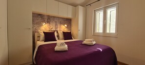 A bedroom with a bed, two bedside lamps, a window with blinds, and a decorative headboard. - Apartments Hvaranin (Stari Grad)