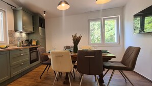 A modern kitchen with green cabinets, a wooden countertop, and a dining area with chairs and a table. - Apartments Hvaranin (Stari Grad)