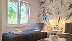 A bedroom with two beds, a window with natural light, a wall with a leaf pattern, and a hanging light fixture. - Apartments Hvaranin (Stari Grad)