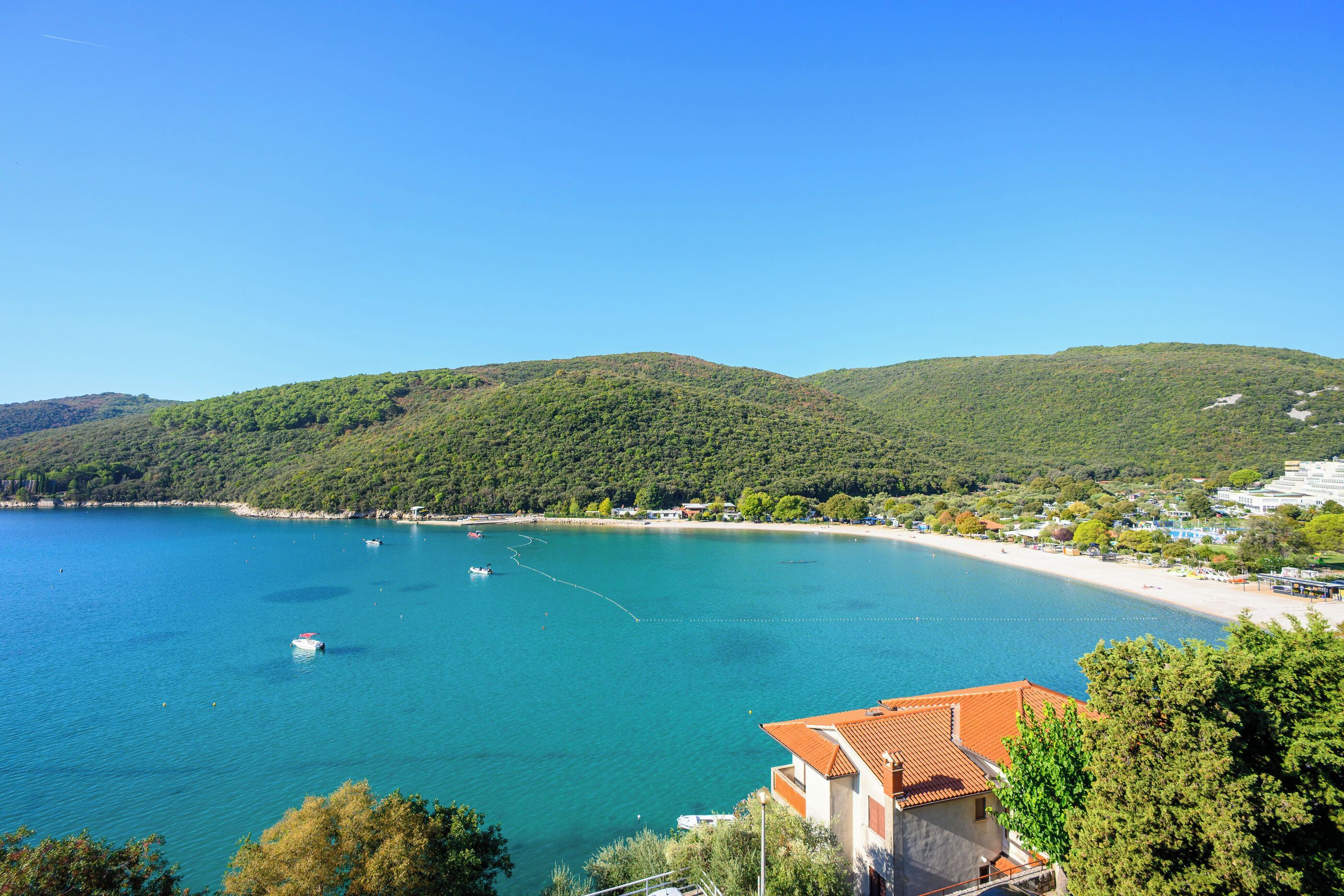 A coastal town with a beach, boats, and hills in the background.