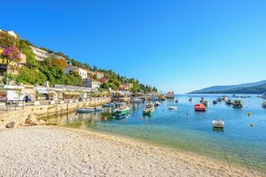A coastal town with a pebbled beach, boats docked along the shore, and buildings with balconies overlooking the water. - Apartment Beautifull View (Labin)