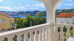 Un balcon offrant une vue sur un paysage côtier, avec des collines et une étendue d’eau.