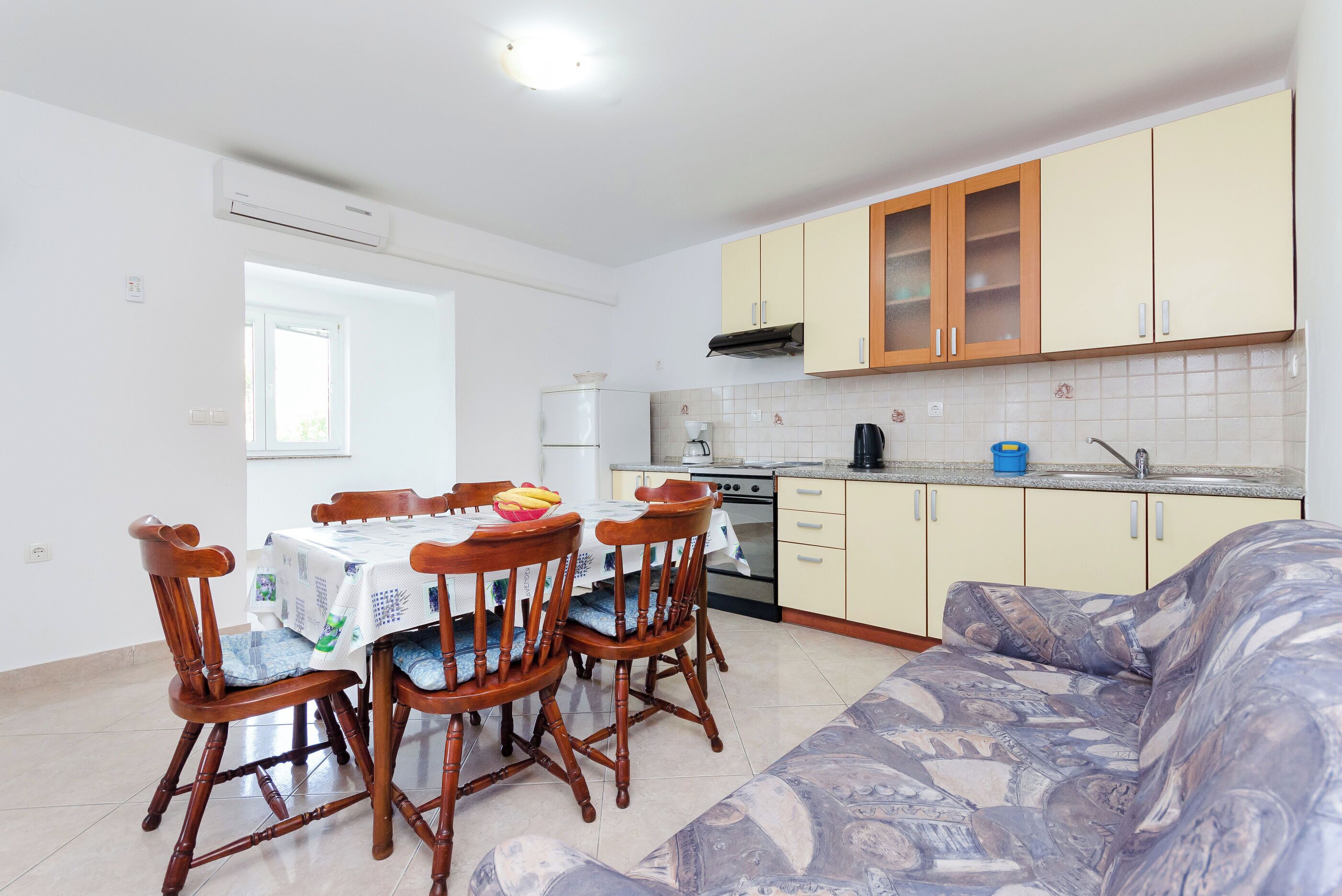 A compact kitchen with a dining area, including a table with chairs, a sofa, and a coffee machine.