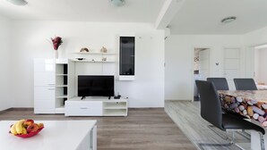 Un salon moderne doté d’un téléviseur à écran plat, de meubles blancs et d’un coin repas avec une table et des chaises.