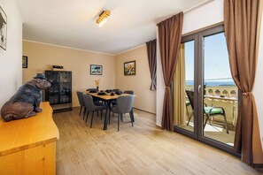 A dining area with a table set for four, a cabinet with a clock, and a statue on a counter. - Apartment Slavko (Rab)