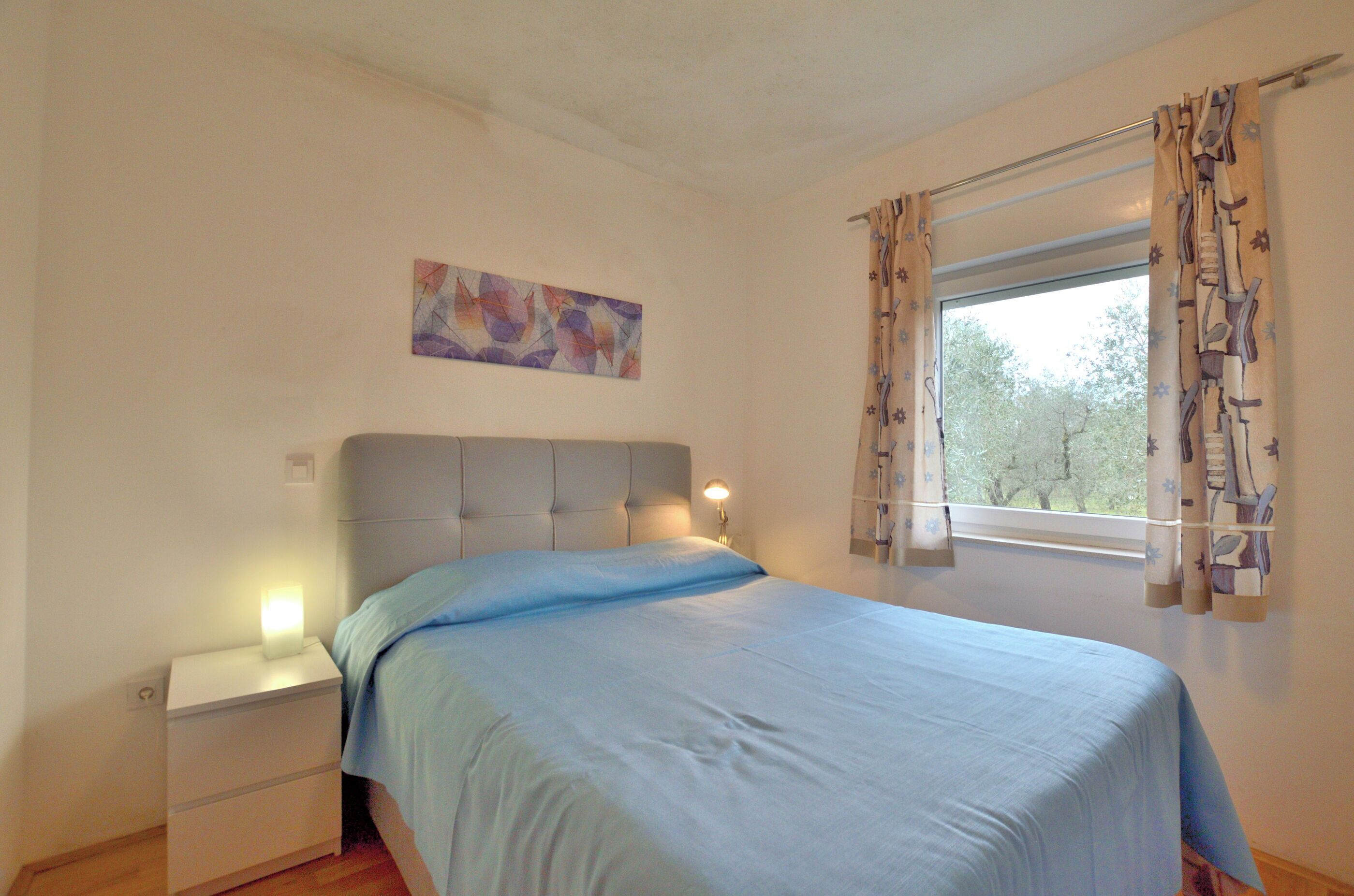 A bedroom with a bed, nightstand, lamp, and window with curtains.