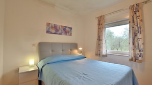 Ein Schlafzimmer mit Bett, Nachttisch, Lampe und Fenster mit Vorhängen.