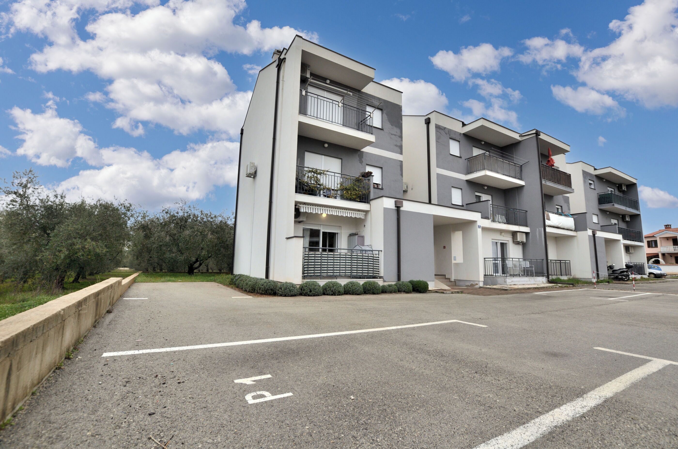 Un edificio residencial de varios pisos con balcones, un estacionamiento y cielo despejado.