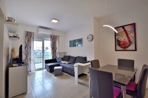 A modern living room with a sofa, a glass dining table, and a TV. - Apartment Amadeo (Fazana)