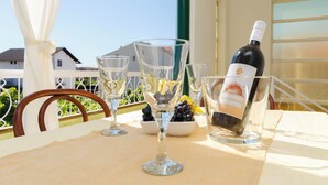 Een tafel met wijnglazen, een fles wijn en een schaal druiven op een balkon met uitzicht op huizen.