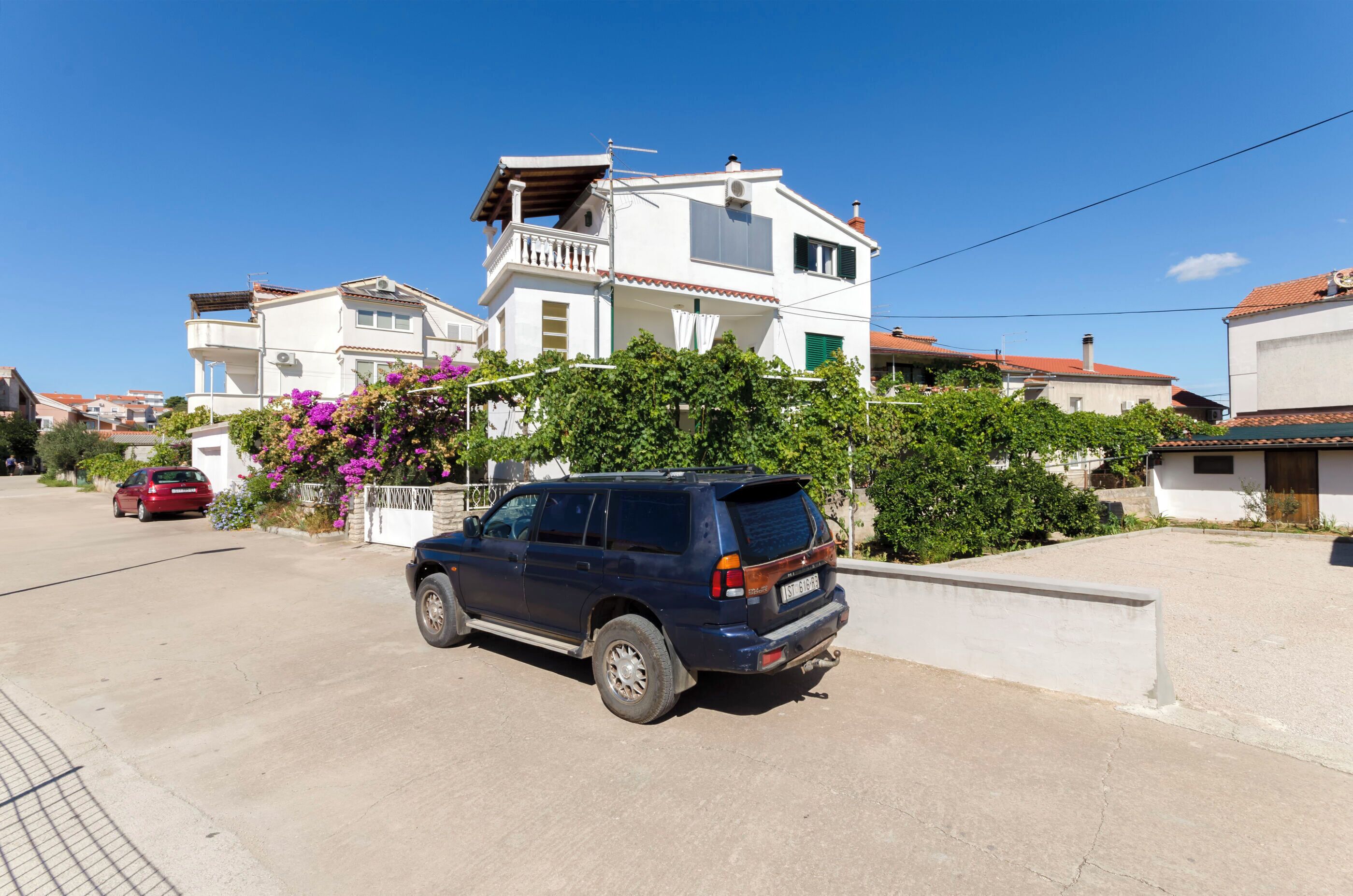 A residential street with houses, a parked blue SUV, and a red car.