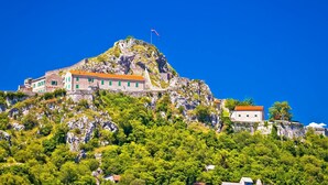 A historic building with a flag on top, situated on a hill with lush greenery. - Apartment Oliva (Knin)