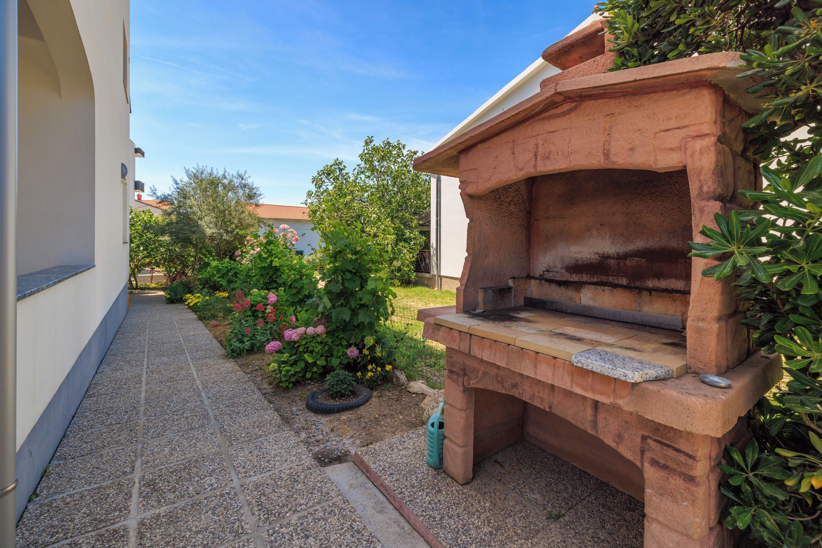 Una griglia in pietra da barbecue in un giardino con un vialetto piastrellato e piante in vaso.