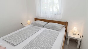 A single-bed room with a wooden headboard, two bedside tables with lamps, and a window with sheer curtains. - Apartments Ivica (Vir)