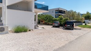 A modern building with a gravel driveway, two parked cars, and a clear blue sky. - Apartments Ivica (Vir)
