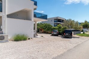 A modern building with a gravel driveway, two parked cars, and a clear blue sky. - Apartments Ivica (Vir)