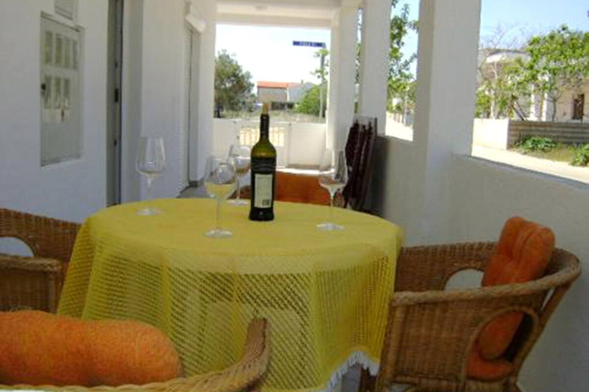 A round table with a yellow tablecloth, surrounded by wicker chairs with orange cushions.