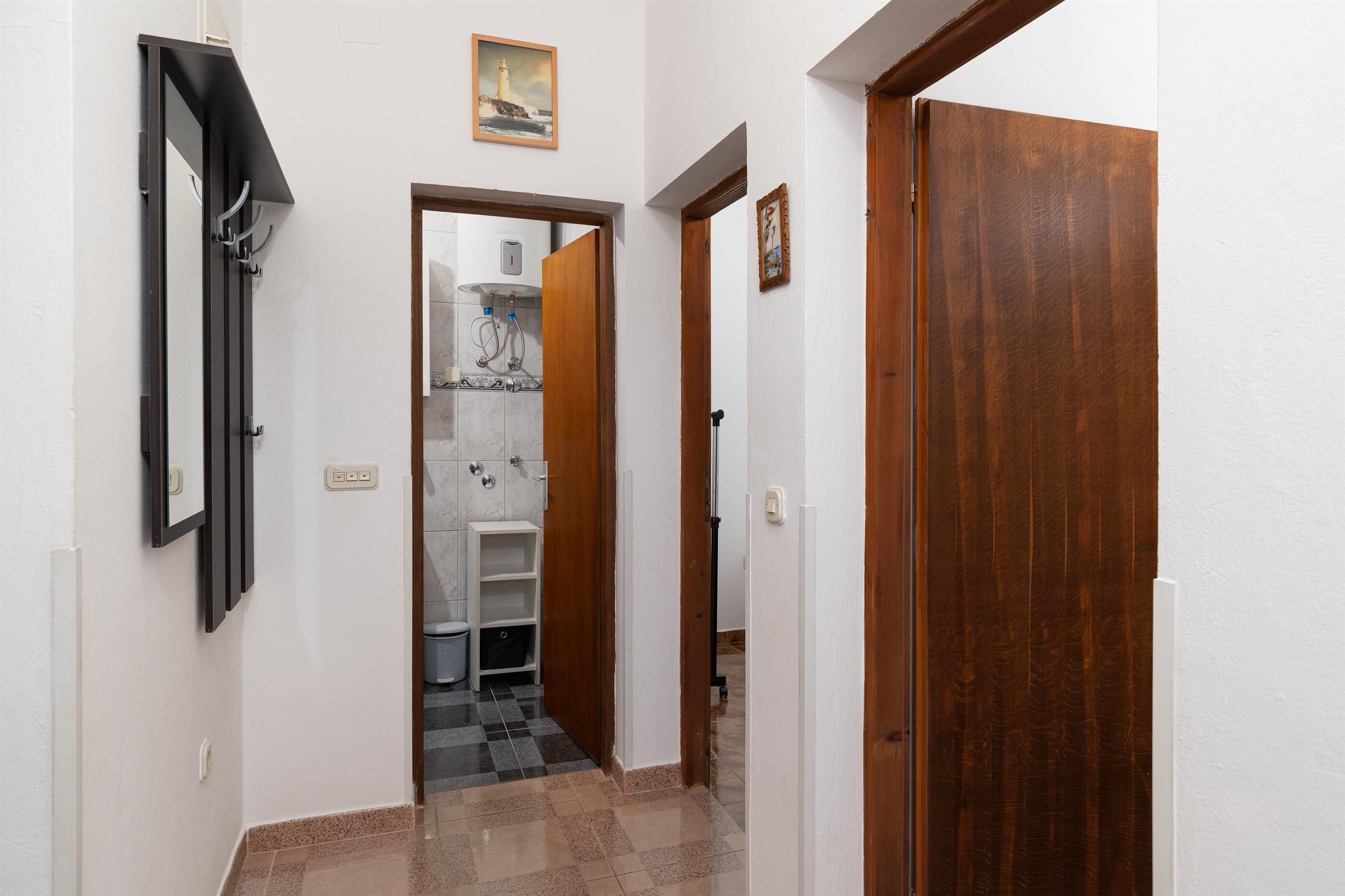 Ein Korridor mit Holztür, weißer Wand und Fliesenboden.