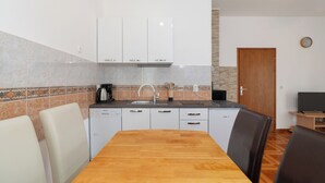 A compact kitchen with white cabinets, a wooden dining table, and a built-in oven. - Apartments Ivica (Vir)