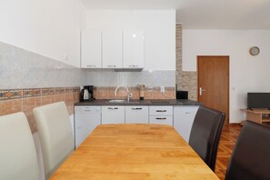 A compact kitchen with white cabinets, a wooden dining table, and a built-in oven. - Apartments Ivica (Vir)
