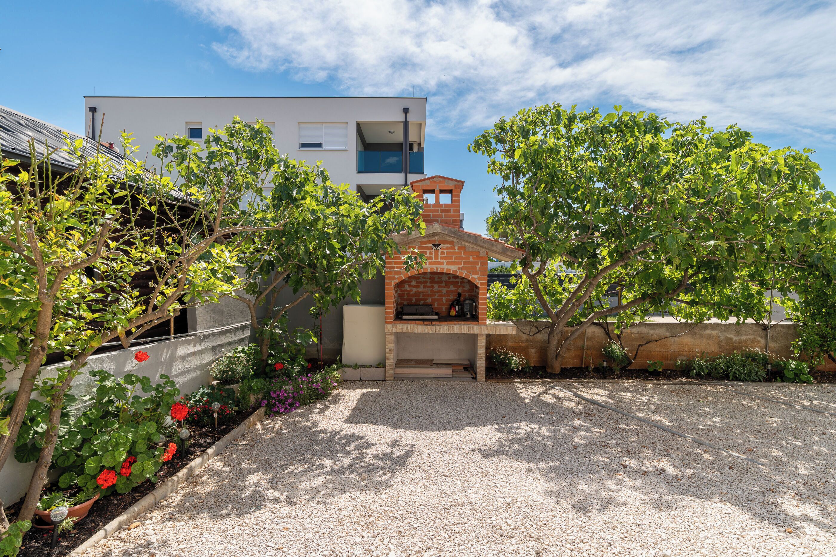 Un bâtiment moderne doté d’un espace barbecue en briques, entour é de gravier et de différentes plantes.