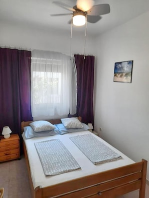 A bedroom with a bed, a ceiling fan, a nightstand, and a wall-mounted picture. - Apartments Ivica (Vir)