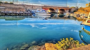 Una marina amb vaixells amarrats, un pont al fons i aigua cristal·lina que reflecteix els voltants.