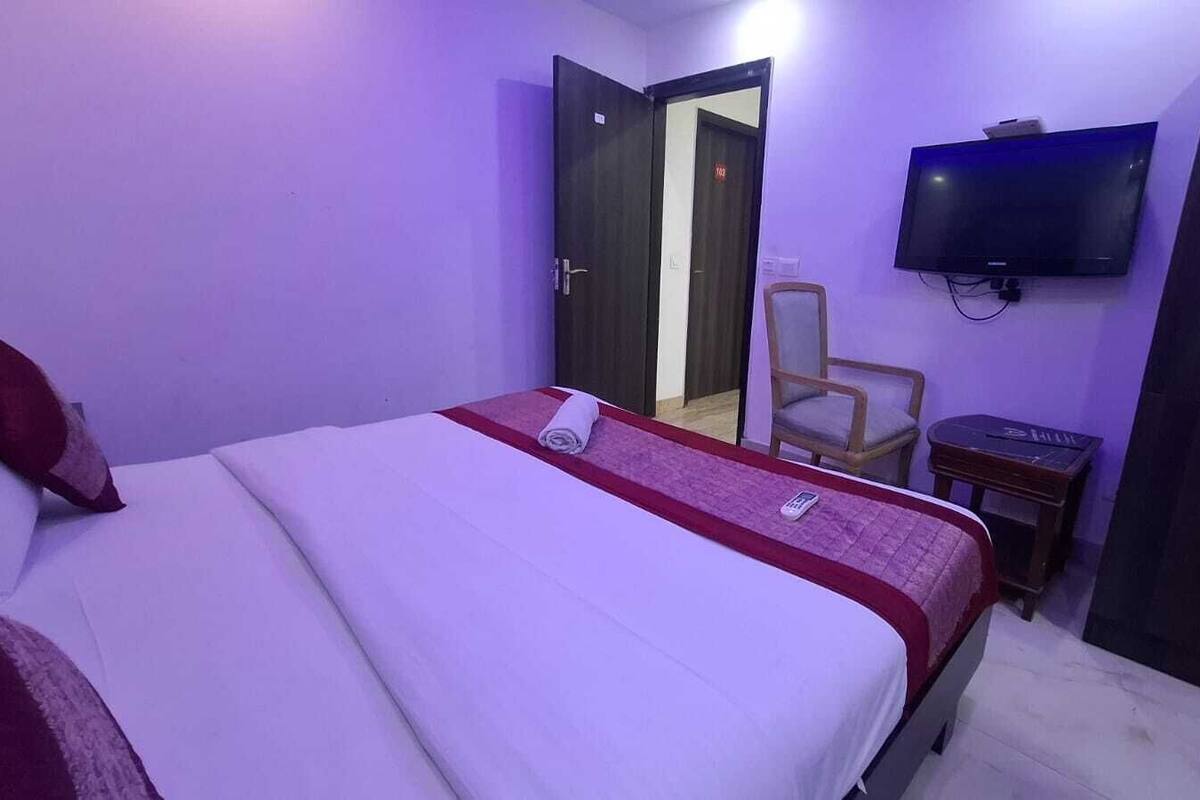 Una habitación de hotel con una cama, televisión montada en la pared, una silla y un armario.