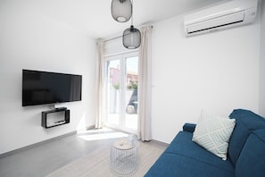 A modern living room with a flat-screen TV, a blue sofa, a small round coffee table, and an air conditioning unit. - House Luxury Konforta (Sibenik)