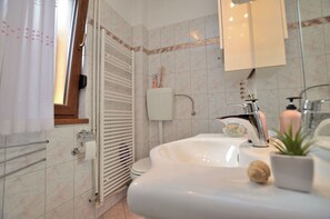 A bathroom with a white sink, a mirror, a towel rack, a toilet, and a shower area. - Apartment Kivi (Fazana)