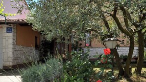 Een appartementencomplex met een stenen gevel, een bord dat het als appartementen aangeeft, en een tuin met rode rozen en diverse planten.