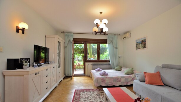 Een kamer met een bed, een bank, een televisie, een kast en een raam met gordijnen.