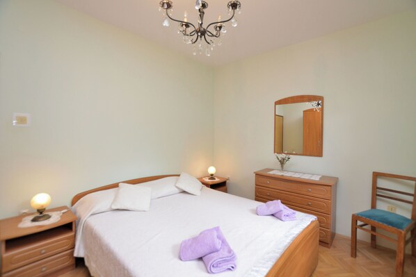 Une chambre à coucher comprenant un lit, des tables de chevet, une commode, une chaise, un miroir et un lustre.