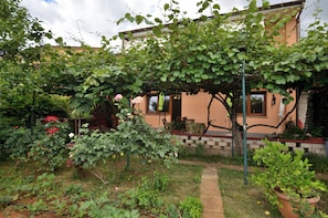 A house with a garden, a pergola with climbing plants, and a brick pathway. - Apartment Kivi (Fazana)
