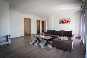 Ein modernes Wohnzimmer mit einem braunen Sofa, einem Couchtisch und einem Teppich. Zwei Türen führen in andere Räume.