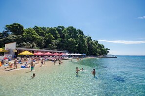 A beach with clear water, umbrellas, and people. - Apartments Biserka G (Rab)