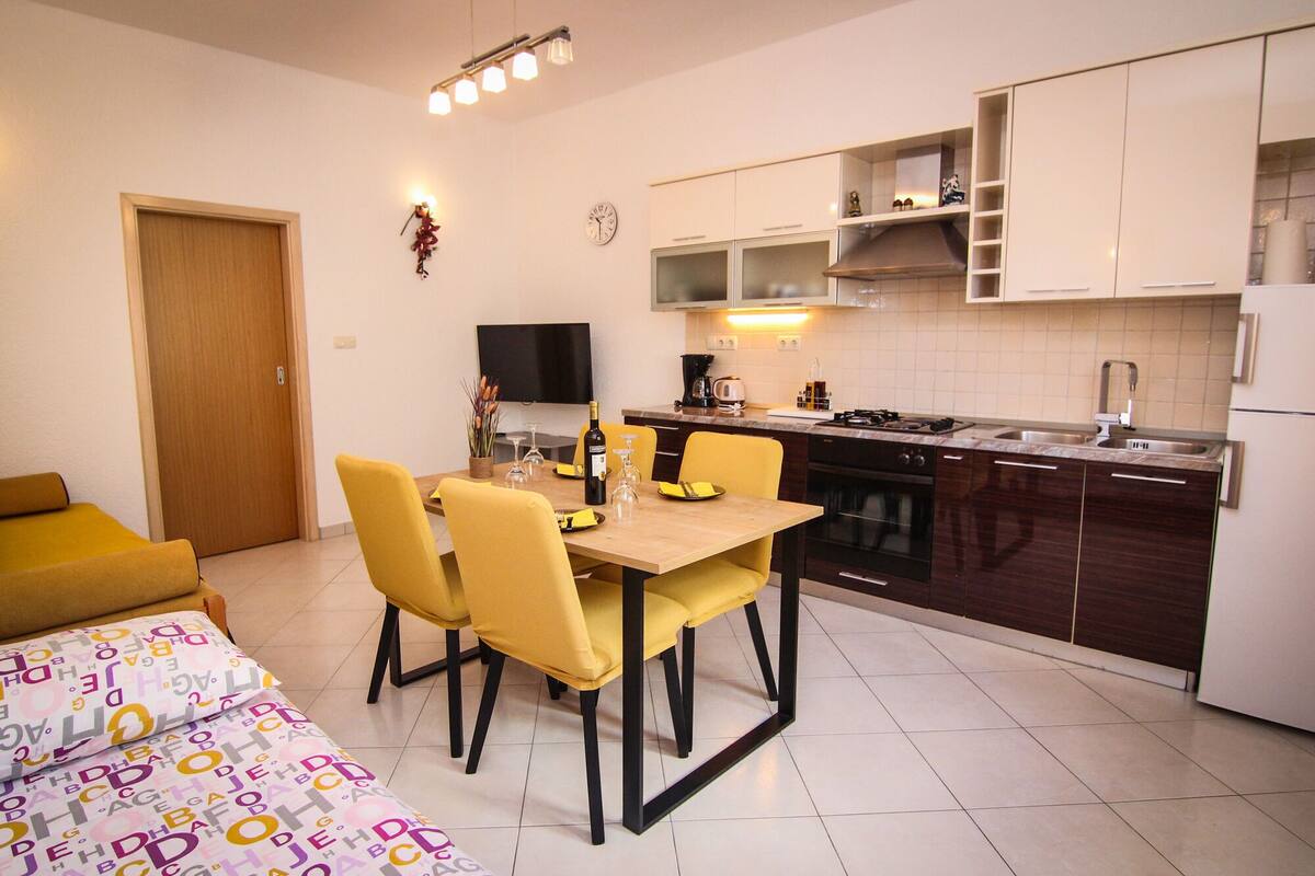 A compact kitchen with a dining area, a TV, and a clock on the wall.