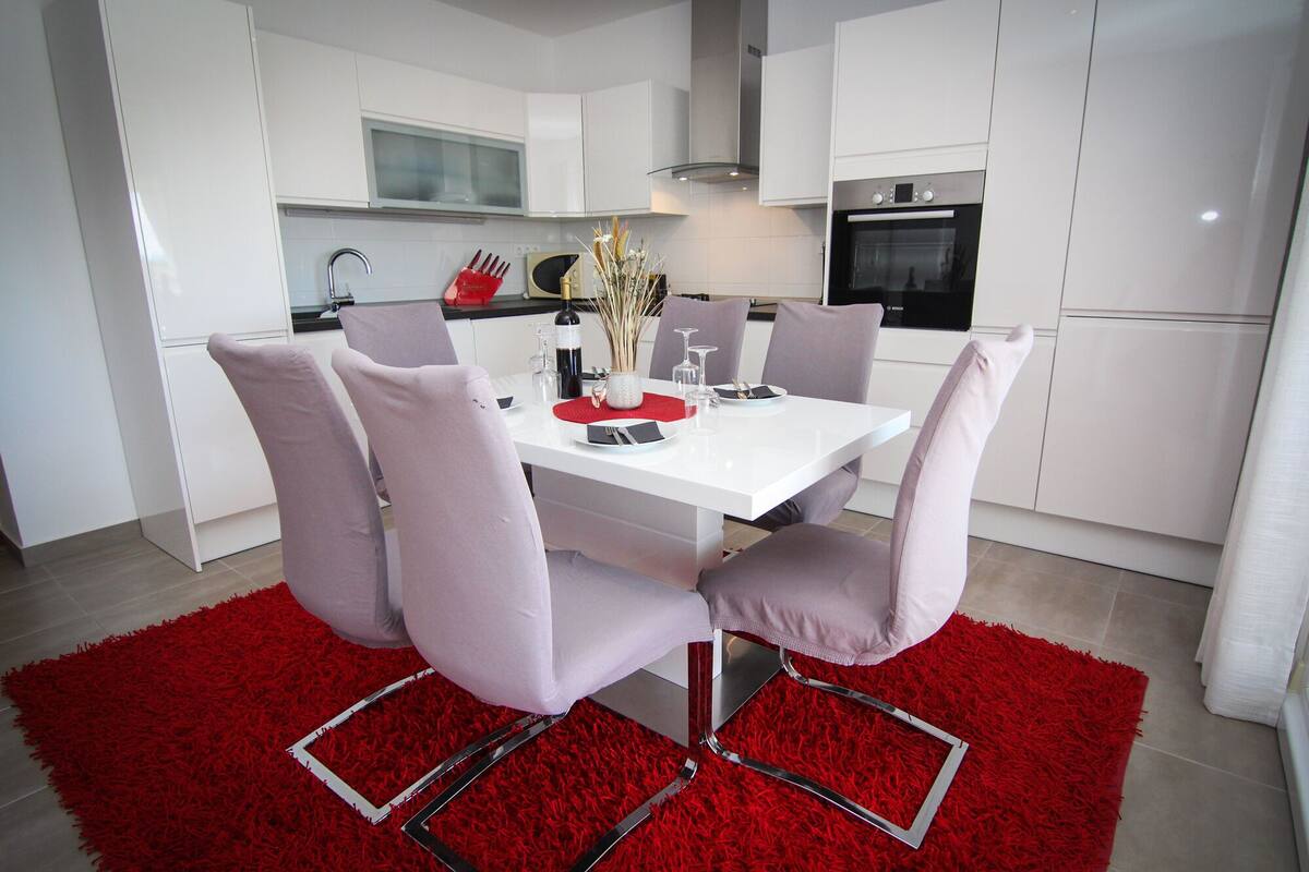 A modern kitchen with white cabinets, a Bosch oven, and a dining table set with chairs.