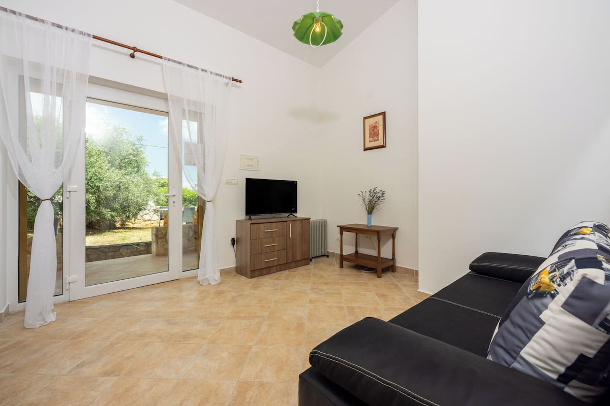 Ein Wohnzimmer mit einer Couch, einem Fernseher, einem Schrank und einer Glastür zum Außenbereich.