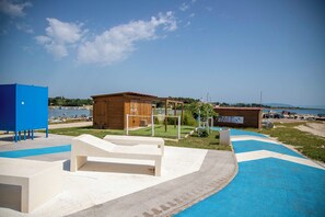 A beachside area with a wooden building, a blue structure, and a white bench. - Apartment David (Liznjan)