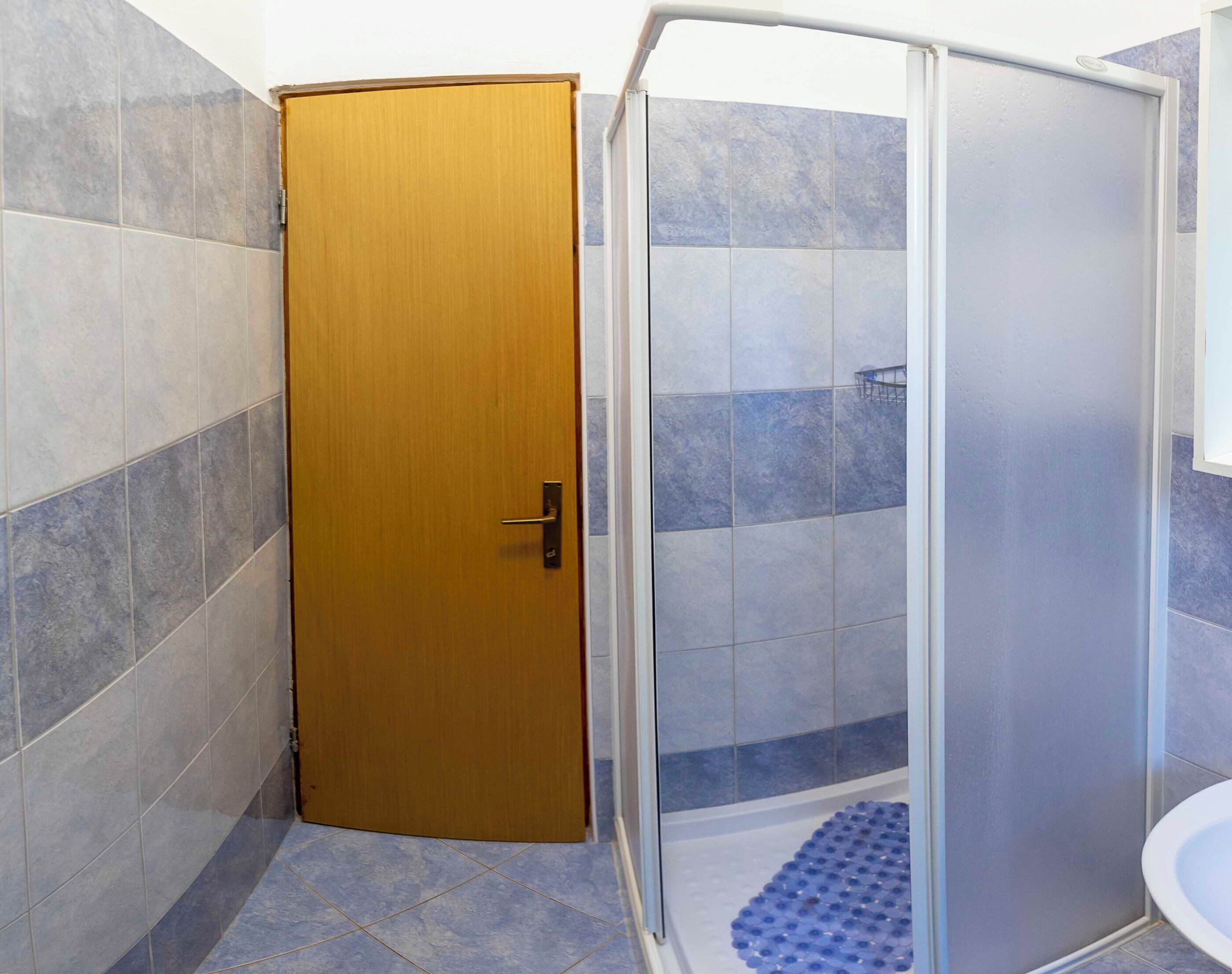 A bathroom with a wooden door, a shower enclosure, and tiled walls.