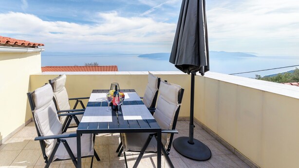 Un balcone con tavolo e sedie, un ombrellone nero e vista sul mare.