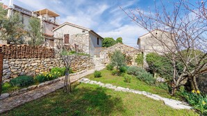Una casa di pietra con giardino, un muro di pietra e cielo sereno.