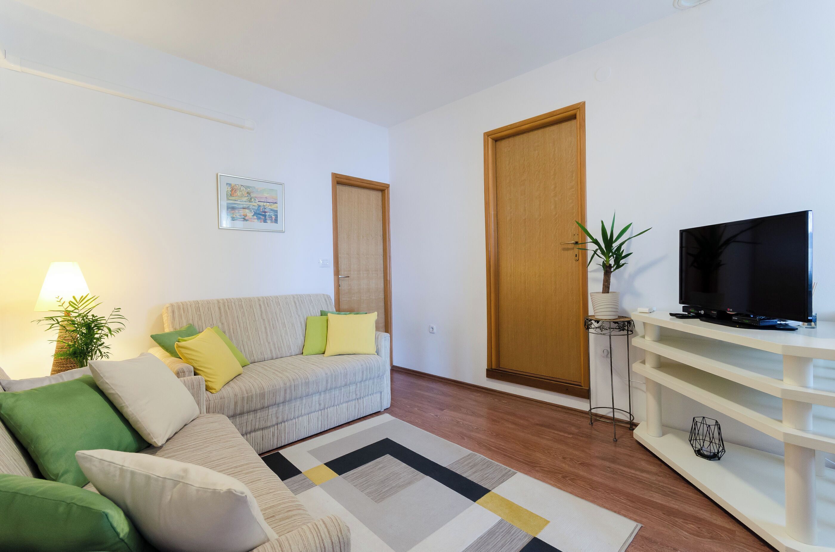 En stue med sofa, tv-møbel og en plante.