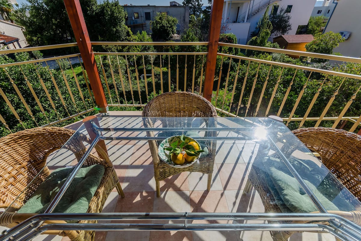 A glass-top table with wicker chairs and a bowl of fruit on a balcony with a metal railing.
