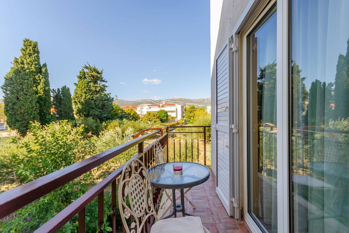 A balcony with a glass door, a round table with a cushion, and a railing.