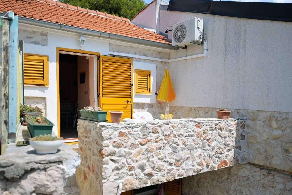 A stone balcony with a white railing, a yellow door, and a small table with potted plants.