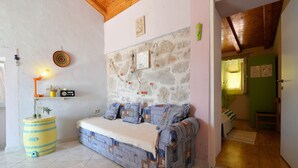 A cozy room with a stone wall, a sofa with patterned cushions, a small shelf with a radio, and a yellow barrel. - Apartments Sunce (Murter-Kornati)