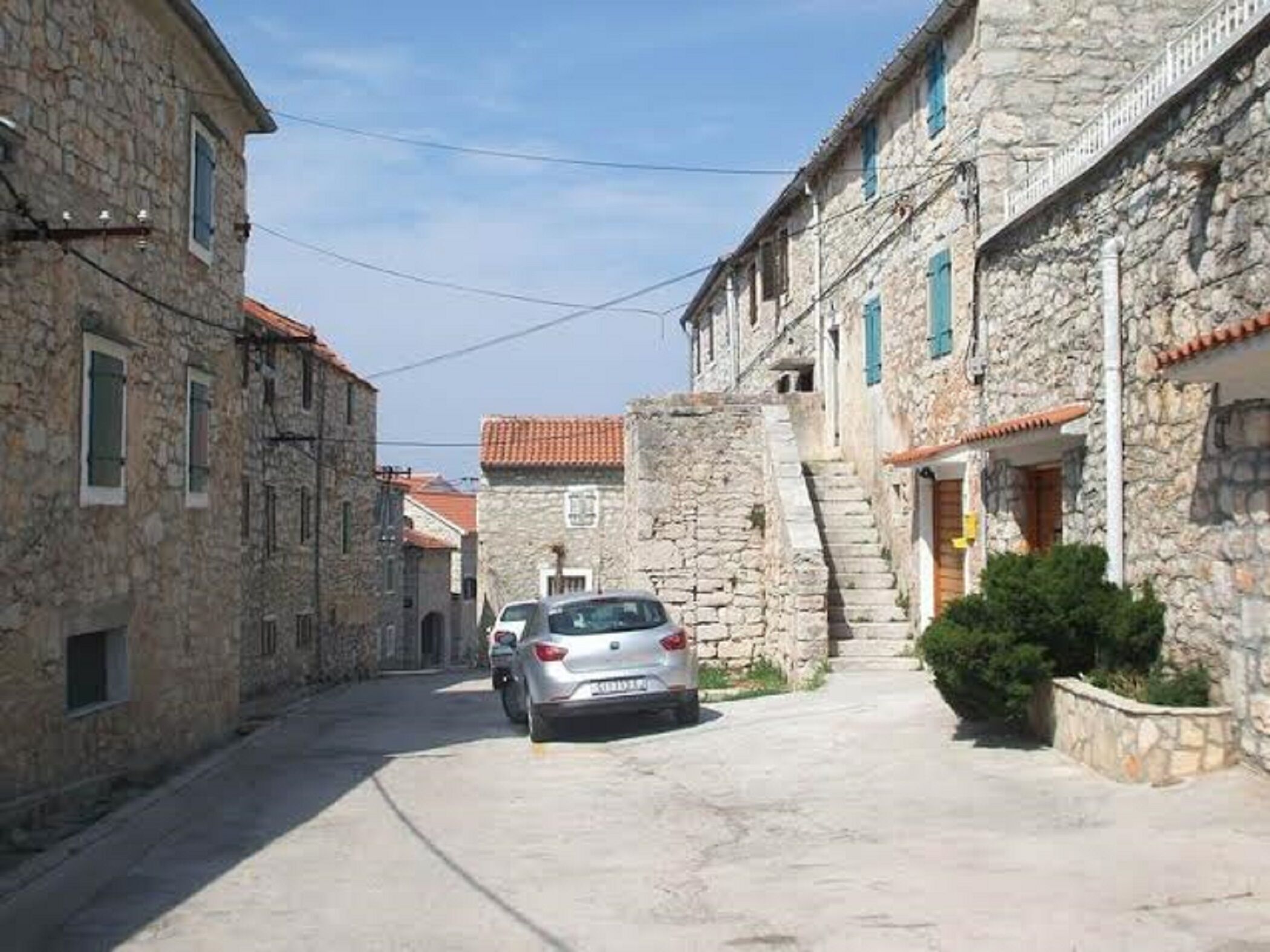 A narrow street lined with stone buildings, a parked car, and a staircase leading to a higher level.